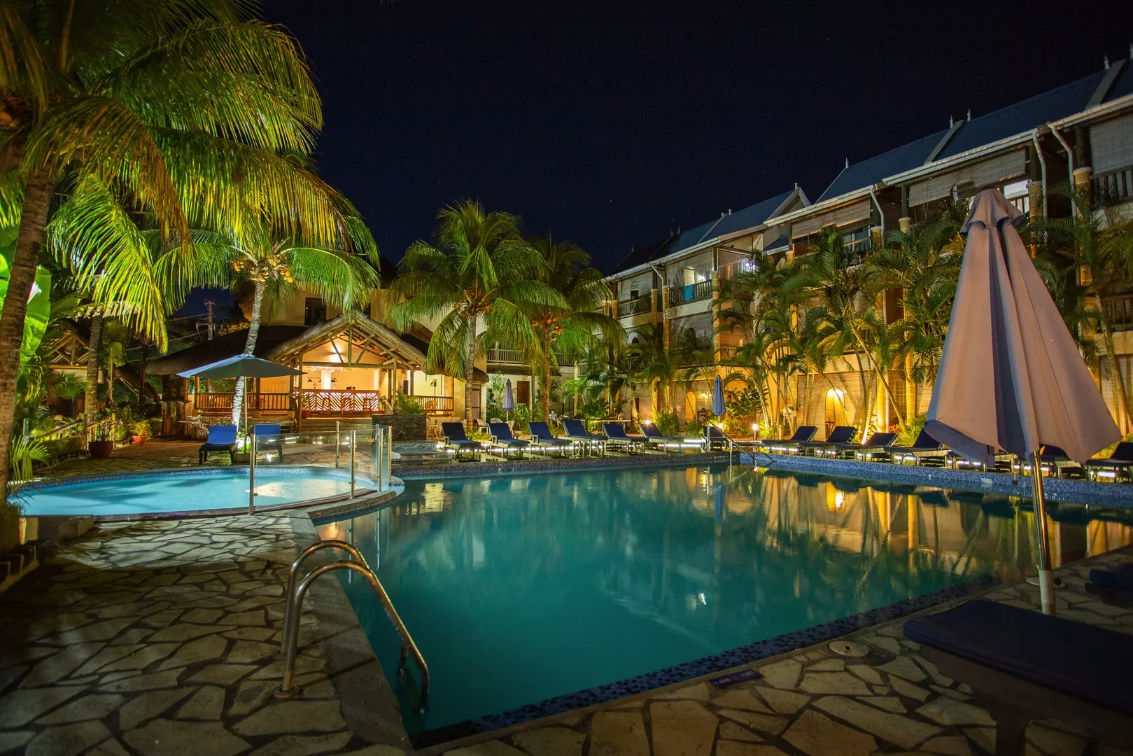 Night view of Le Palmiste Resort & Spa with illuminated swimming pool and tropical palm trees