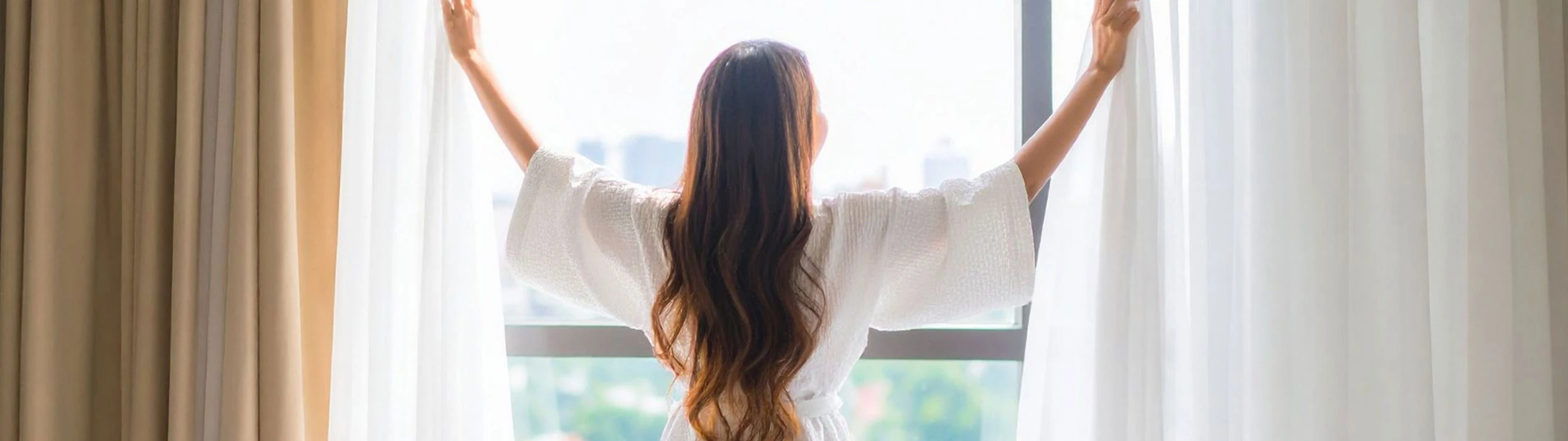 Guest opening the curtains in a bright and comfortable room at Le Palmiste Hotel, starting the day with a serene view